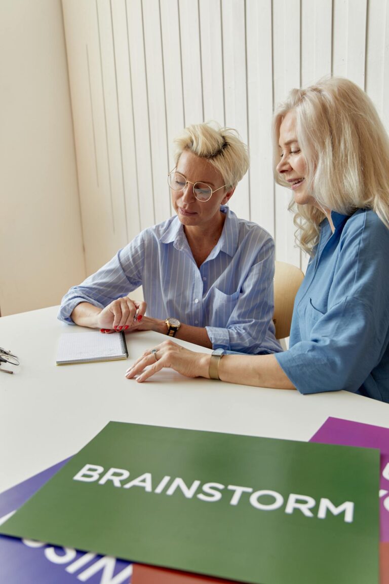 Two elderly women engaging in a brainstorming session at a business meeting with placards on the table.