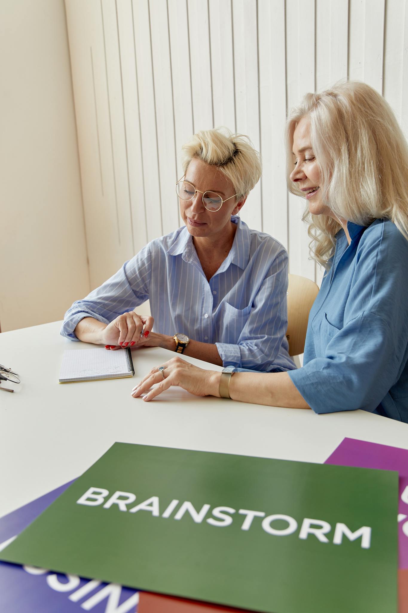 Two elderly women engaging in a brainstorming session at a business meeting with placards on the table.